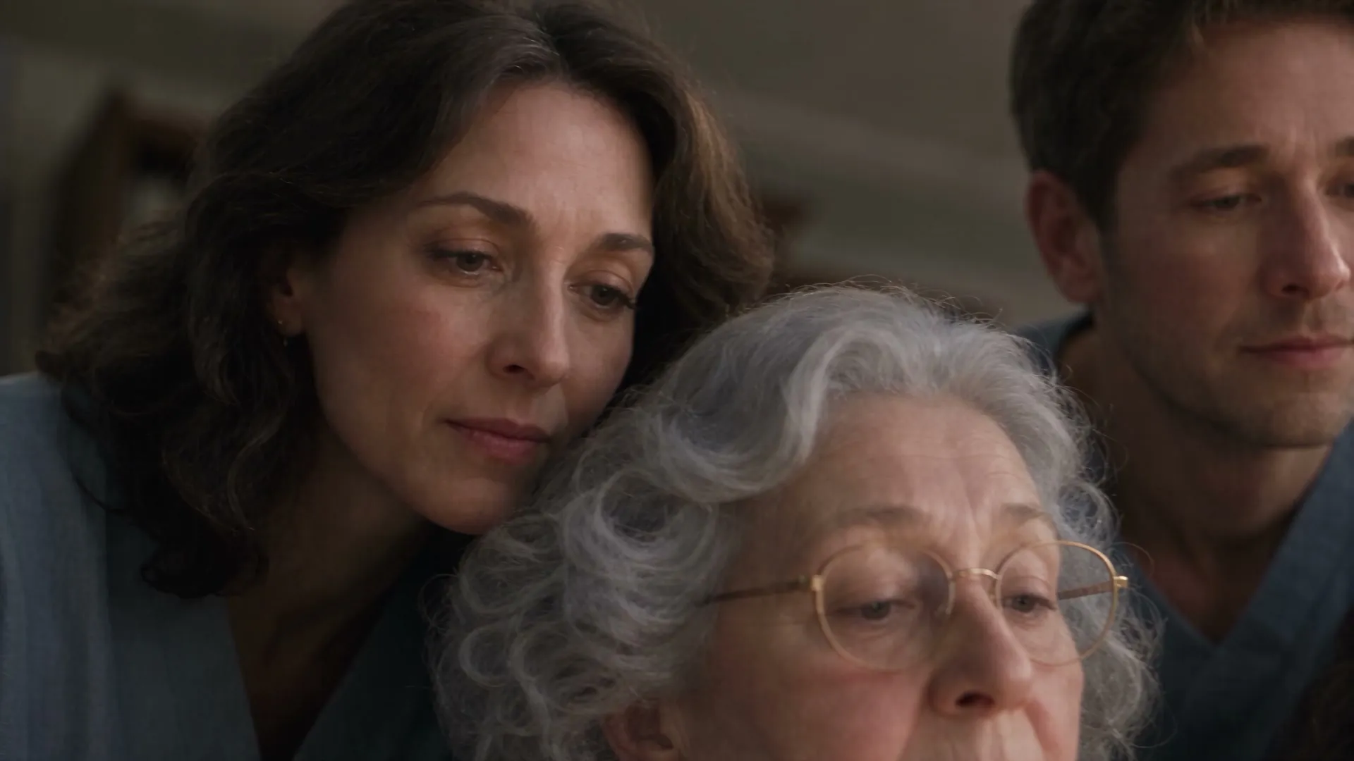 A woman resting her head against a grandmother's as they and a young man look down together