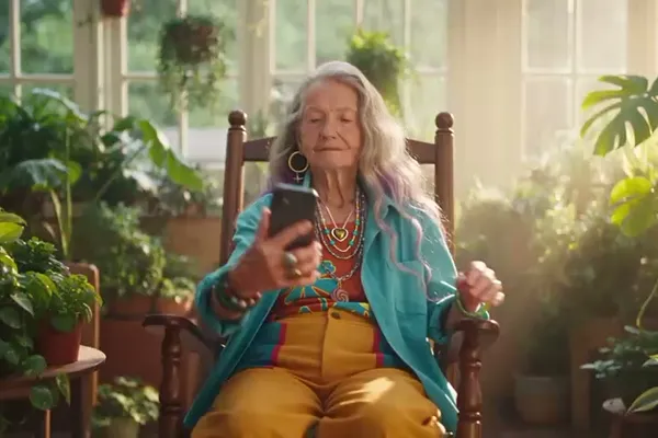 An older woman taking a selfie in her sunroom and smiling at her RiBi avatar on the phone